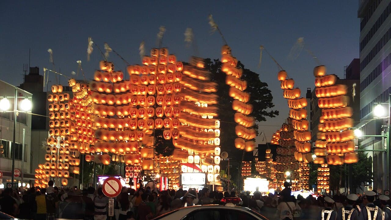 Illuminated bamboo kanto poles balanced on performers at night during the Akita Kanto Festival