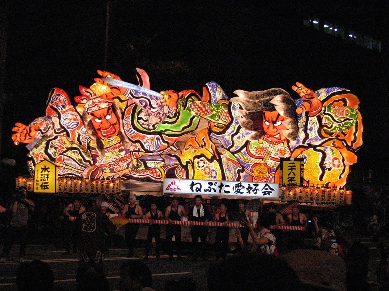 A giant illuminated warrior nebuta float glowing at night during the Aomori Nebuta Matsuri parade