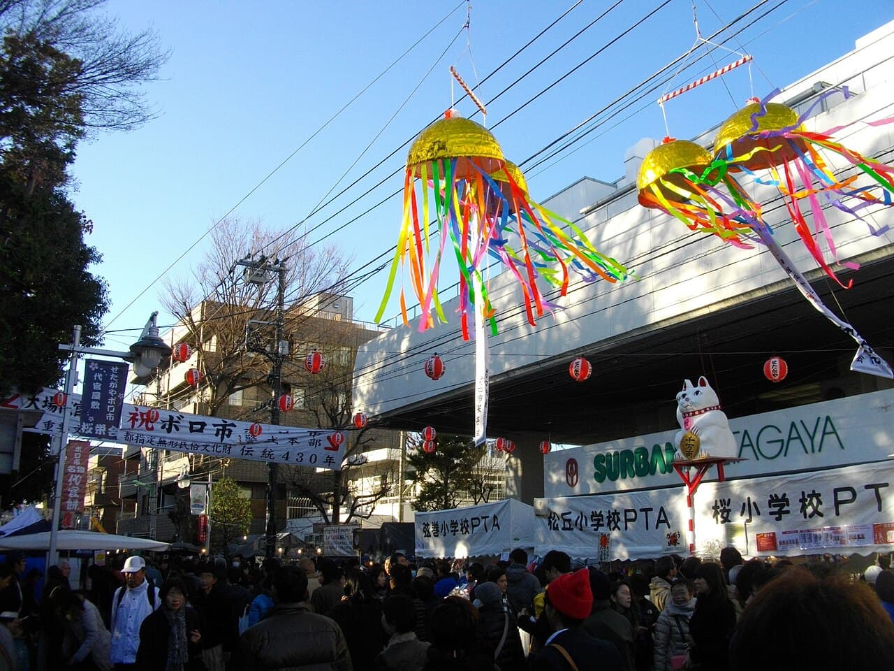 Kusudama decorations and a 'Boro-ichi' banner above a street crowded with visitors and white stall tents at the Setagaya Boro-ichi flea market, Setagaya, Tokyo (photographed December 2012)
