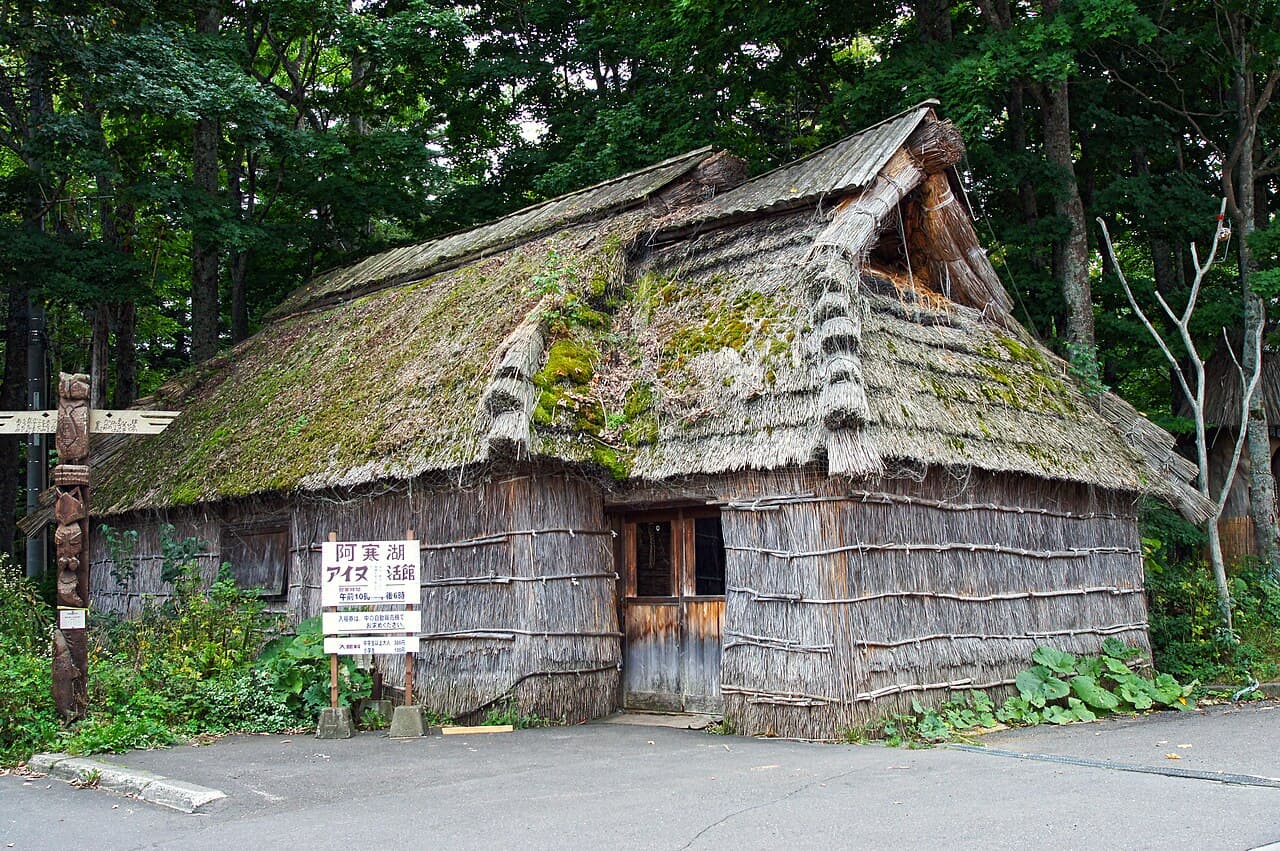 A traditional thatched-roof Ainu chise house and carved wooden post at Akanko Ainu Kotan, the festival's venue