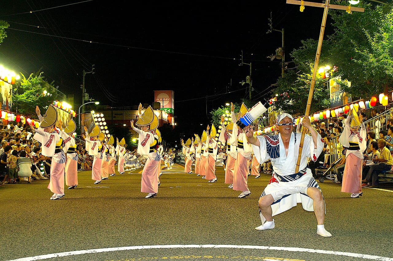 Awa Odori dancers in formation at night on a lantern-lined street with a seated crowd, Tokushima
